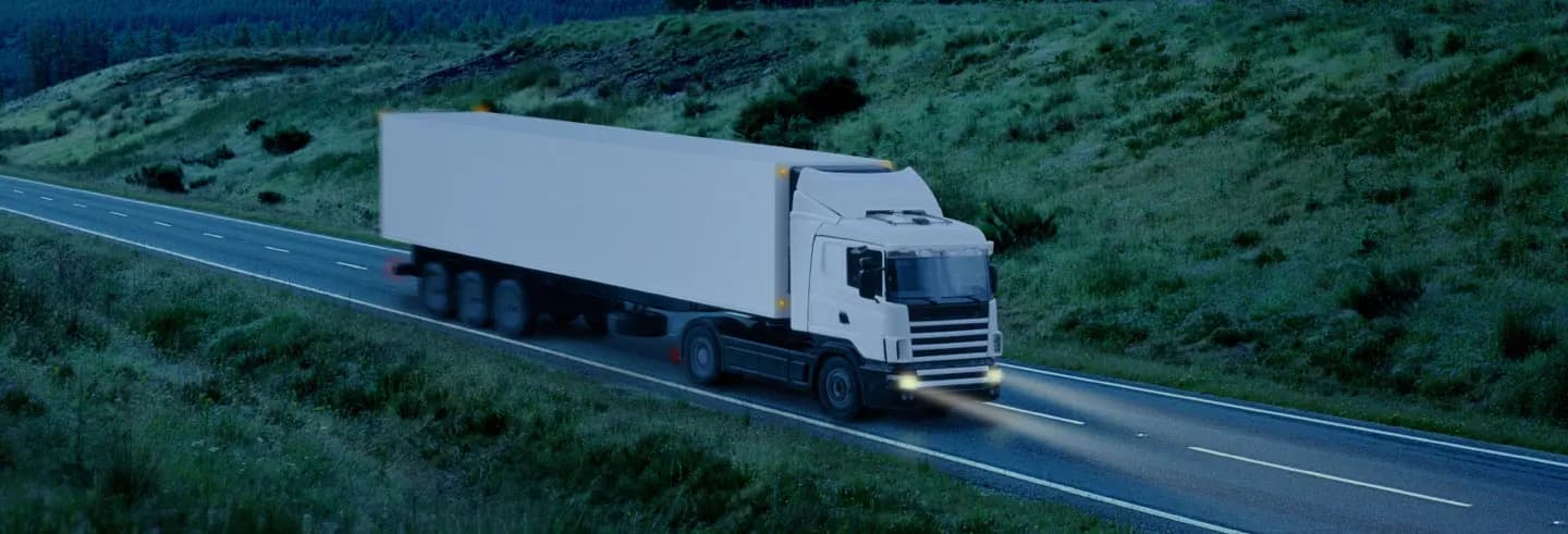Truck driving down a highway through green hills at dusk