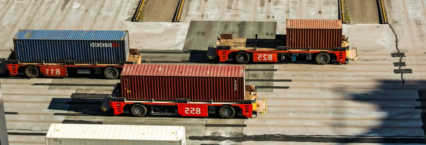 Aerial view of shipping containers being moved across a terminal yard