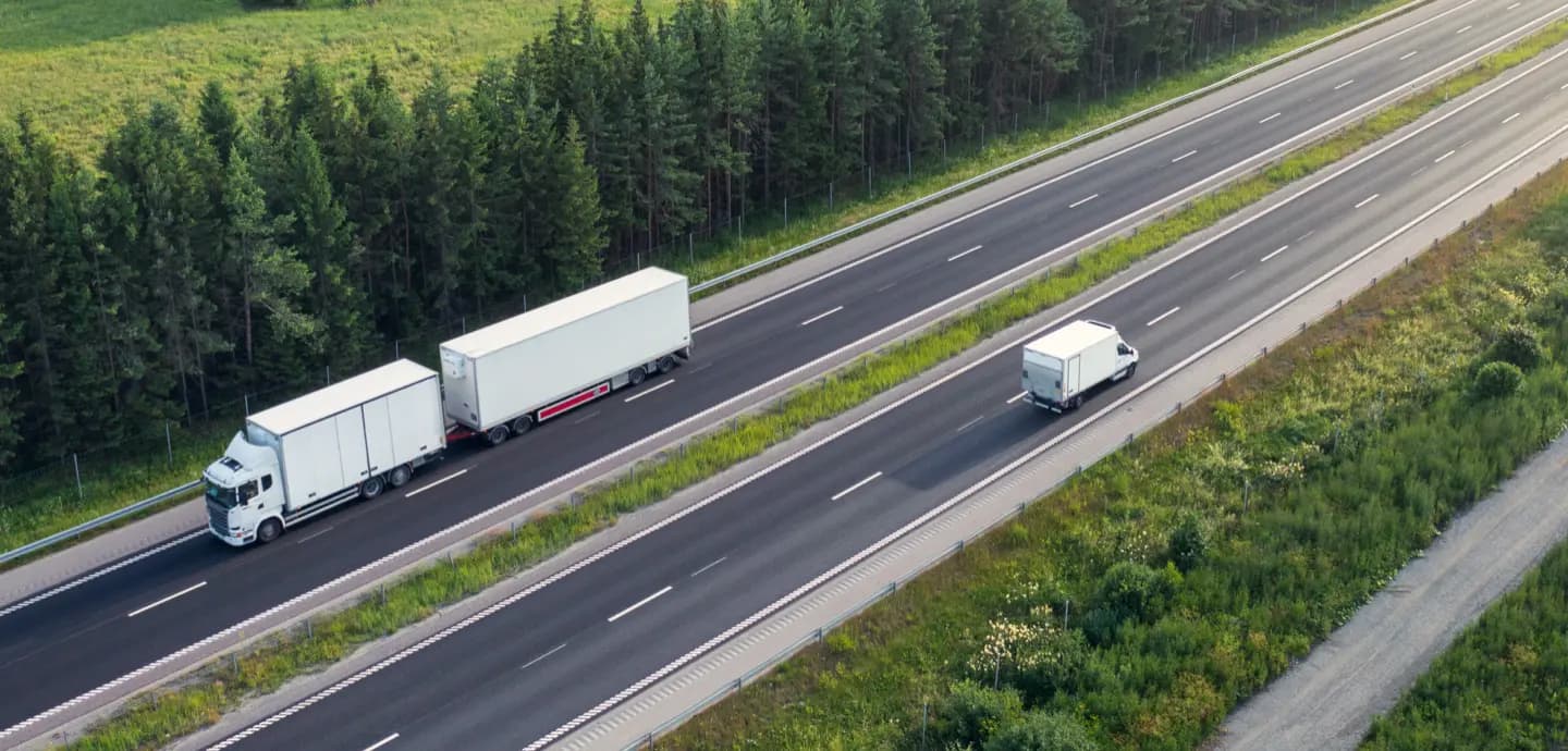 Aerial view of trucks driving on a highway alongside a forest